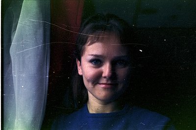 Close-up portrait of a young woman with blue eyes and auburn hair, wearing a dark blue sweater. Visible film grain and scratc...