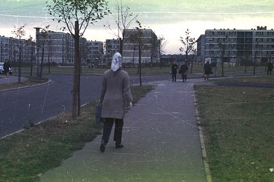 A man walks along a paved path in a modernist housing complex, likely Eastern European, with large, blocky apartment building...