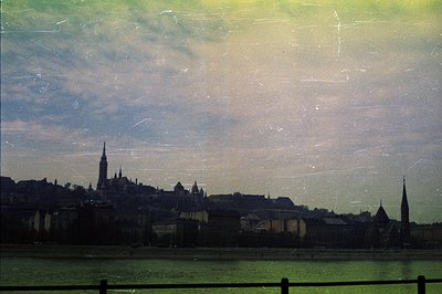 Dramatic, aged view of a European cityscape, likely Budapest, Hungary, featuring a castle hill skyline punctuated by spires a...