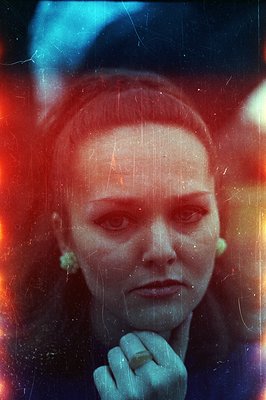 Close-up portrait of a woman with a short haircut and green earrings. Strong color cast—red, blue, and yellow—indicates exper...