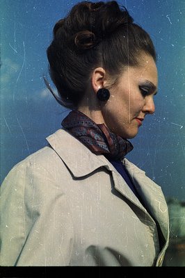 Profile portrait of a woman in a light trench coat, adorned with a patterned scarf and statement earrings. Her hair is styled...