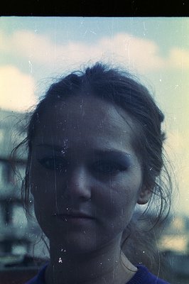 A solemn portrait of a young woman with a pensive expression, captured in a heavily scratched film photograph. Noticeable fil...