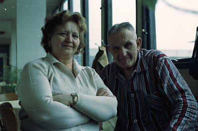 A middle-aged couple poses indoors near a large window, showcasing retro clothing styles and hairstyles common in the 1970s. ...