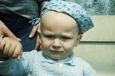 A young child, likely a toddler, looks directly at the camera, wearing a blue and white floral-patterned hat. They are dresse...