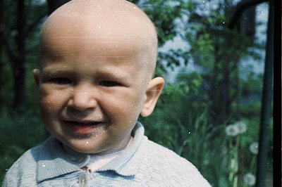 Close-up portrait of a baby with a broad smile, wearing a light blue knit sweater. Visible film grain & scratches suggest age...