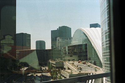 Architectural view of a modern convention center with a distinctive curved white roof, flanked by high-rise office buildings....