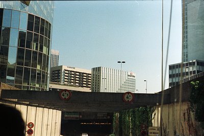 Urban landscape featuring modern office buildings and a raised highway overpass. Visible signage includes "La Défense" and sp...