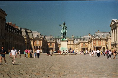 Grand view of the Palace of Versailles' courtyard. Elaborate Baroque architecture with statues, fountains, and crowds of tour...