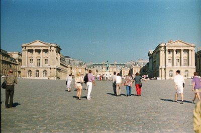 Palace of Versailles, France. Wide, paved courtyard framed by symmetrical buildings with classical columns. Numerous tourists...