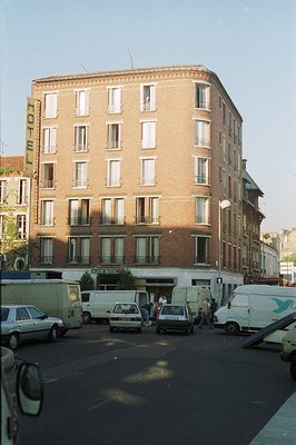 A multi-story brick hotel with a corner entrance and prominent "Hotel" signage. Several older vehicles, including vans and se...