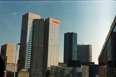 Several modernist office towers dominate the skyline. "TOTAL" signage prominently displayed atop two buildings, likely corpor...