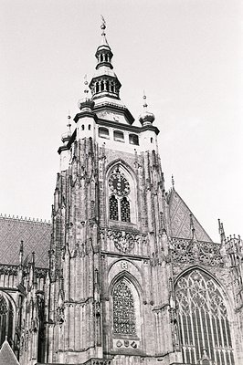 Striking black and white image of a Gothic cathedral tower. Elaborate stonework, pointed arches, and a central clock face are...