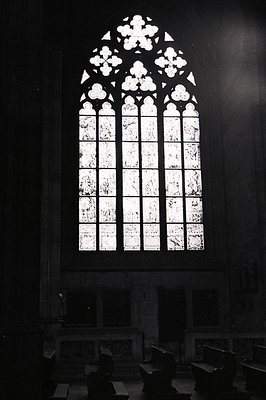 High-contrast black and white image showcasing a large, ornate Gothic window. Detailed tracery creates a pointed arch above a...