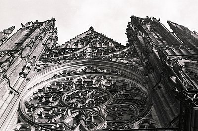 Dramatic, upward view of a Gothic cathedral facade. Intricate rose window dominates, framed by pointed arches and complex tra...