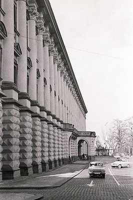 Monumental facade of a building with a repeating pattern of Corinthian columns and arched openings. Cobblestone street with v...