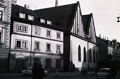 Black and white photo showing a historic European townscape. Features timber-framed buildings with steeply pitched roofs, nar...