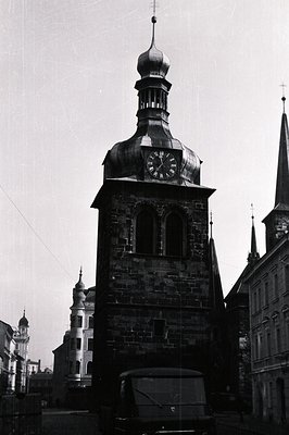 A tall, stone clock tower dominates the frame, featuring a distinctive dome and visible clock face. Surrounding structures in...