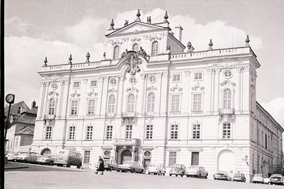 Elegant Baroque palace facade features symmetrical design, prominent central balcony, and elaborate cornices. Cars from the 1...