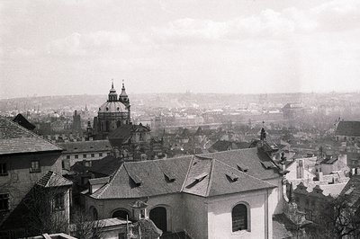 Elevated view showcasing a historic cityscape, likely Prague. Distinctive Baroque church dome dominates the skyline above til...