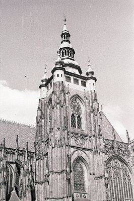 A tall, ornate church tower with a clock face dominates this monochrome image. Gothic architecture features intricate stonewo...