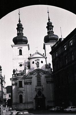 Striking monochrome captures a Baroque-style church facade with two distinctive onion-domed towers. Statues flank the entranc...