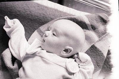 Infant, likely under a year old, rests on a textured blanket, wearing a simple white garment. A side profile emphasizes their...