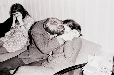 A tightly framed, intimate portrait shows a man embracing a woman, while another woman sits nearby, visibly distressed, wipin...