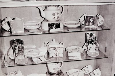 Elegant china set displayed on tiered shelves within a cabinet. Features teacups, saucers, a teapot, and bowls adorned with f...