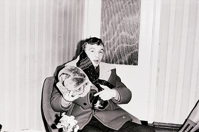 A young man in a dark coat and patterned scarf poses playfully, pointing towards the camera with an exaggerated expression. H...
