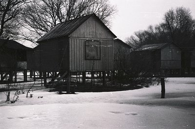 Elevated, wood-frame structure with a gabled roof sits on stilts amidst a snow-covered landscape. Similar structures are visi...
