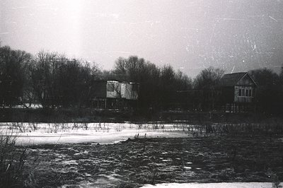 A stark, black and white landscape featuring a traditional wooden structure, possibly a farmhouse or barn, set within a snowy...