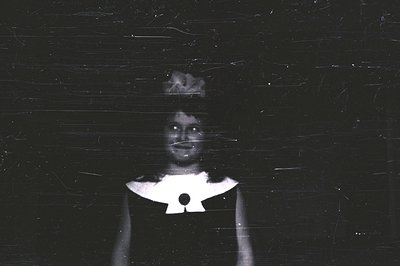 Close-up portrait of a young woman wearing a dress with a prominent, stylized collar. The image shows noticeable film grain a...