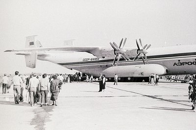 A Soviet-era Antonov An-12 turboprop aircraft, registration number СССР-64459, stands on an airfield apron. A crowd of onlook...
