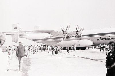 An Antonov An-12 transport aircraft (registration CCCP-64459) sits on an airfield apron. A crowd of onlookers, mostly women i...