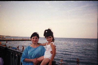 A woman and young girl pose on a promenade overlooking the Black Sea. The woman wears a light blue shawl; the child wears a w...