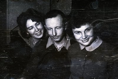 Three individuals, likely friends, are closely posed for a candid portrait. Visible attire suggests a casual, mid-century sty...