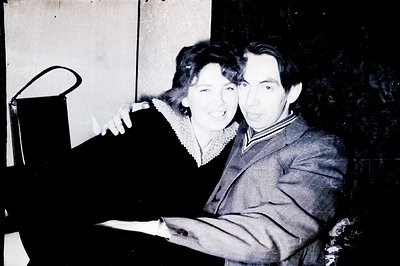 A black and white portrait of a couple, likely 1960s or 1970s. The woman wears a dark dress with lace collar, and the man a t...
