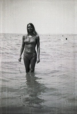 A young woman stands waist-deep in shallow water, facing the camera. She wears a dark bikini. The monochromatic image, likely...