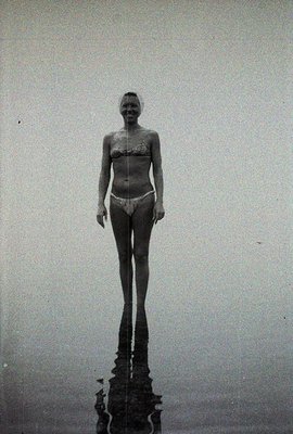 A woman stands knee-deep in water, viewed from below, showcasing a vintage swimwear style. The monochromatic image highlights...