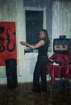 A young woman stands presenting to a screen displaying a DVD menu. She's dressed in black trousers and a dark top. A vibrant ...