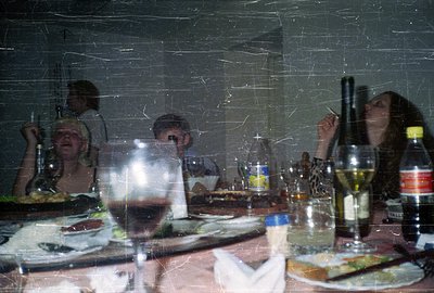 A candid snapshot captures a group gathered around a table laden with food and drink. Appears to be a candid moment with evid...
