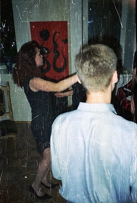 A man in a white shirt embraces a woman in a black dress, positioned in front of a vibrant abstract painting. Interior scene ...