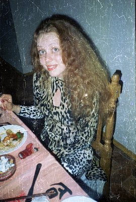 A young woman with long, wavy blonde hair sits at a table with a meal. She wears a patterned, low-cut top. Visible food inclu...