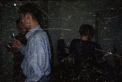 Two figures are seen in profile, illuminated by a flashlight. The man in blue jeans and a light blue shirt holds the light so...