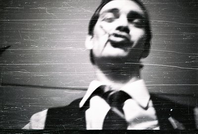 Close-up portrait of a man in a suit and tie, appearing to address an audience. The image exhibits strong directional lightin...