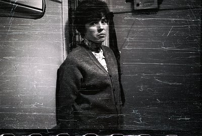 A striking portrait of a woman in a dark sweater and a bob haircut. The monochrome image, with visible film grain and scratch...