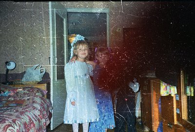 Two young girls in matching pale blue, sequined dresses stand in what appears to be a home interior, likely a hallway or entr...