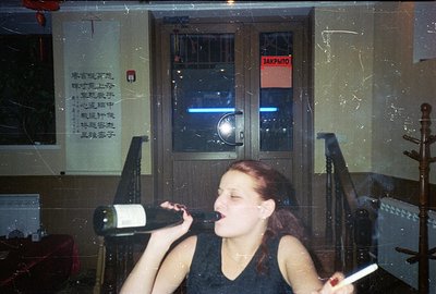 A woman, mid-action, is shown drinking directly from a bottle of red wine. The backdrop features a closed door marked "Закрыт...