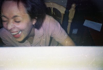 A person with short dark hair, wearing a light pink shirt, leans forward with their eyes closed and mouth open in apparent la...
