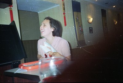 A young woman with short, dark hair laughs while seated at a table, likely in a Chinese restaurant. She wears a pink top and ...